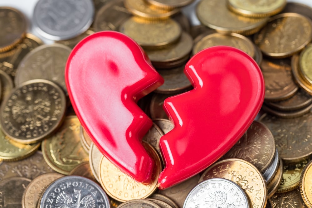 two halves of a pink plastic heart resting on a bunch of coins