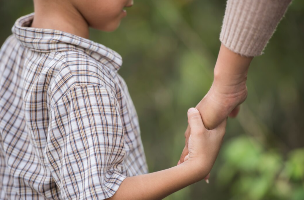 The child in the shirt holds the hand of a person, forest on a blurred background