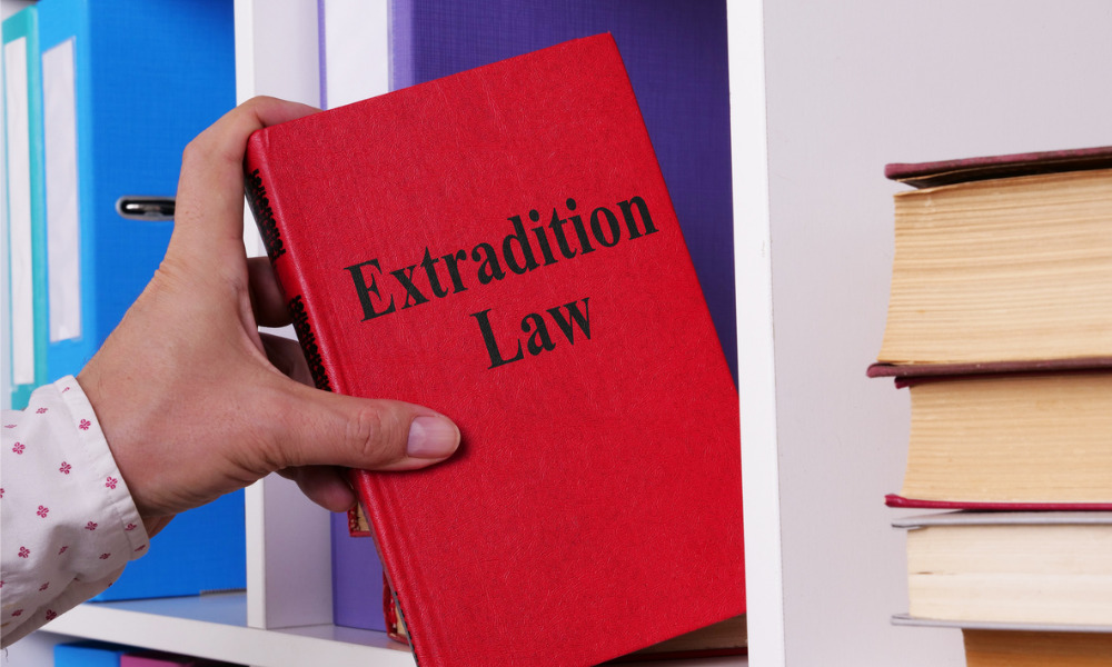 a hand holding a book labeled “Extradition Law